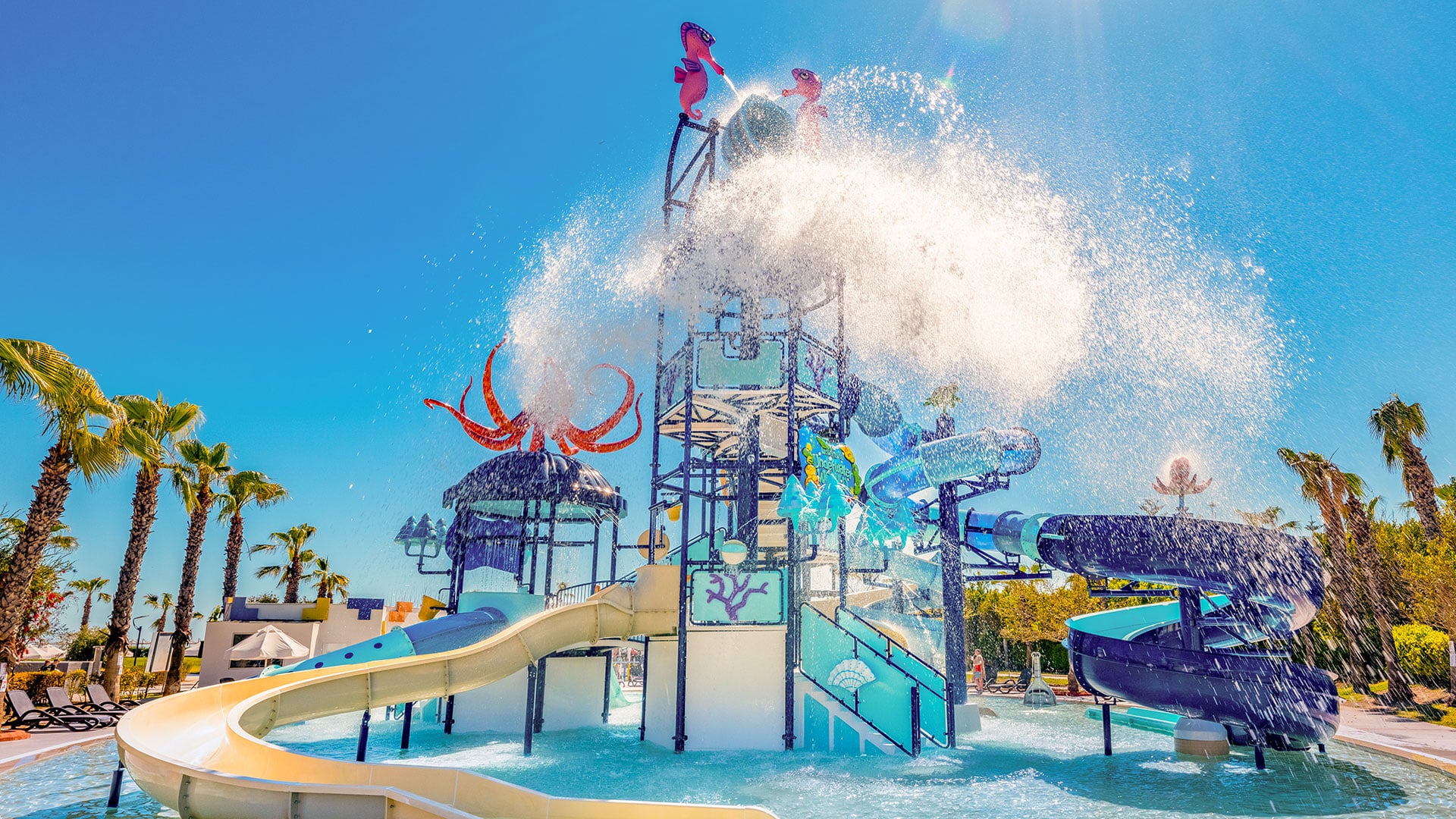 http://Parc%20aquatique%20pour%20enfants%20avec%20toboggans%20et%20jeux%20d'eau,%20décoré%20avec%20des%20motifs%20de%20la%20mer%20et%20des%20palmiers.