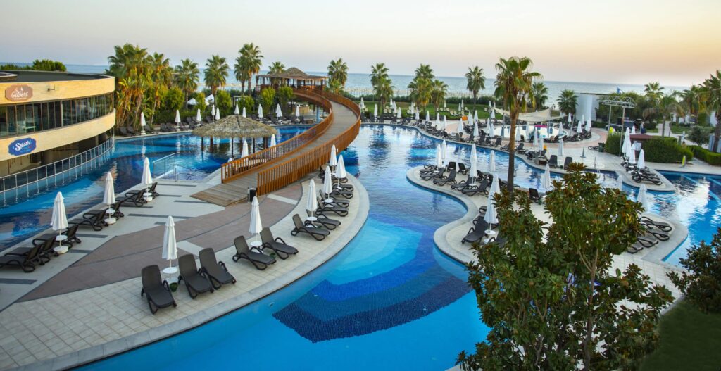 Grande piscine entourée de palmiers avec des chaises longues et des parasols au bord de l'eau.