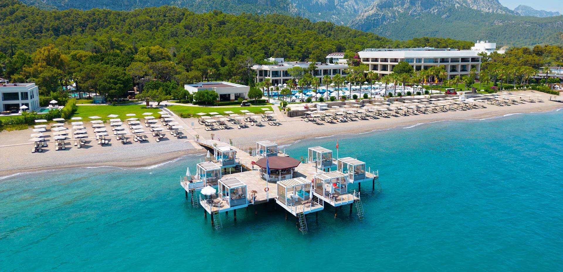 http://Vue%20aérienne%20d'un%20complexe%20hôtelier%20en%20bord%20de%20mer%20avec%20une%20plage%20de%20sable%20aménagée%20et%20des%20piscines%20entourées%20de%20palmiers.