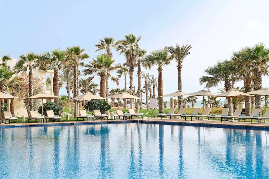 http://Piscine%20extérieure%20entourée%20de%20palmiers%20sous%20un%20ciel%20dégagé
