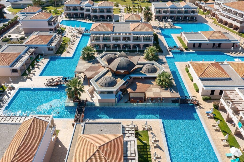 Vue aérienne de l'hôtel entouré de piscines, bâtiments avec toits en tuiles rouges.